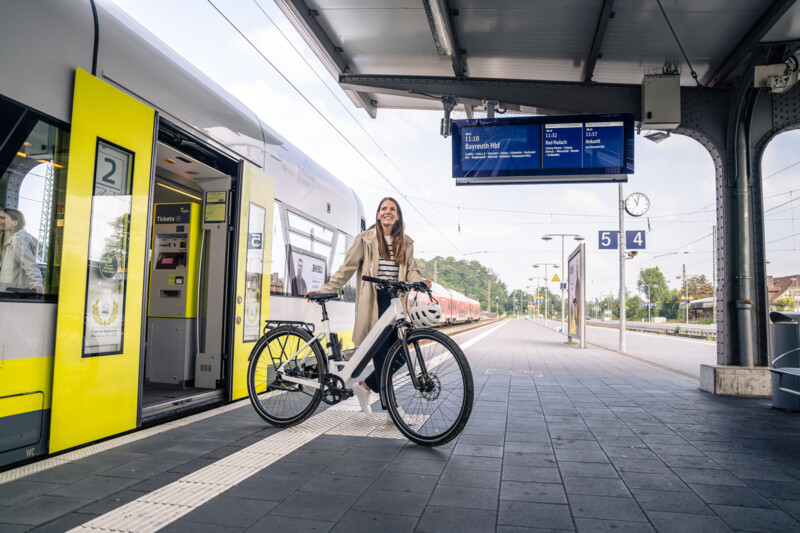 A woman is standing on the platform next to an open regional train with an e-bike.